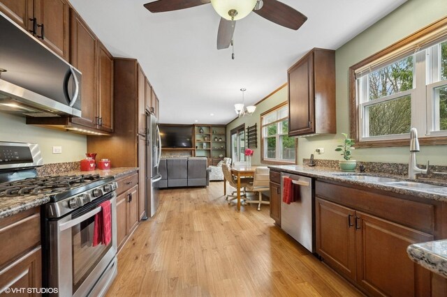 kitchen with a sink, dark stone countertops, light wood-type flooring, ceiling fan, and appliances with stainless steel finishes