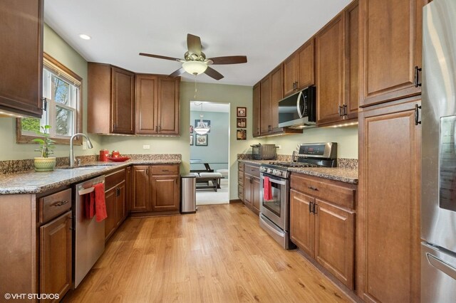 kitchen featuring a ceiling fan, a sink, light wood-type flooring, brown cabinetry, and appliances with stainless steel finishes