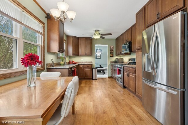 kitchen featuring light wood-style flooring, a sink, ceiling fan with notable chandelier, light stone countertops, and appliances with stainless steel finishes