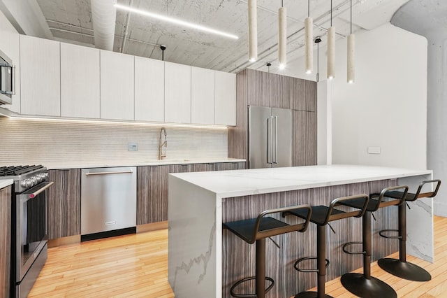 kitchen with light wood-style floors, a kitchen bar, tasteful backsplash, a sink, and stainless steel appliances