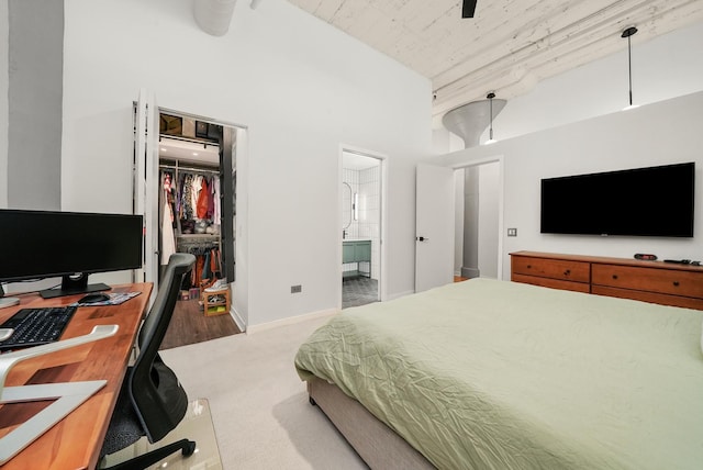 bedroom with a towering ceiling, a closet, ensuite bathroom, a walk in closet, and light colored carpet