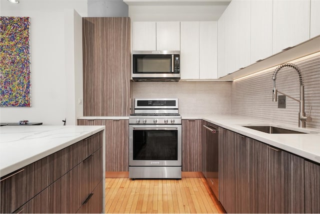 kitchen with a sink, decorative backsplash, stainless steel appliances, light wood-style flooring, and light stone counters