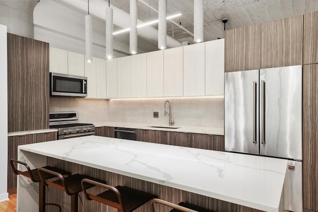 kitchen featuring tasteful backsplash, modern cabinets, a sink, stainless steel appliances, and a breakfast bar area