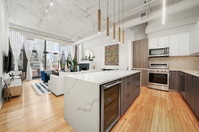 kitchen featuring visible vents, modern cabinets, light wood-style floors, wine cooler, and stainless steel appliances