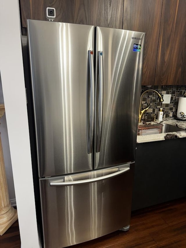 details with backsplash, freestanding refrigerator, dark brown cabinetry, a sink, and dark wood-style floors
