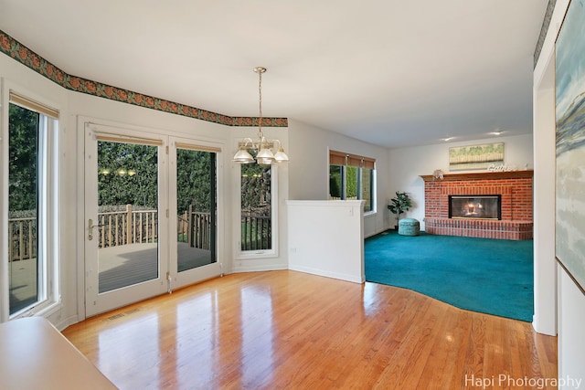 unfurnished living room featuring baseboards, an inviting chandelier, a brick fireplace, visible vents, and wood finished floors