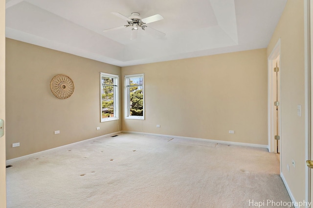 empty room featuring carpet, ceiling fan, baseboards, and a raised ceiling
