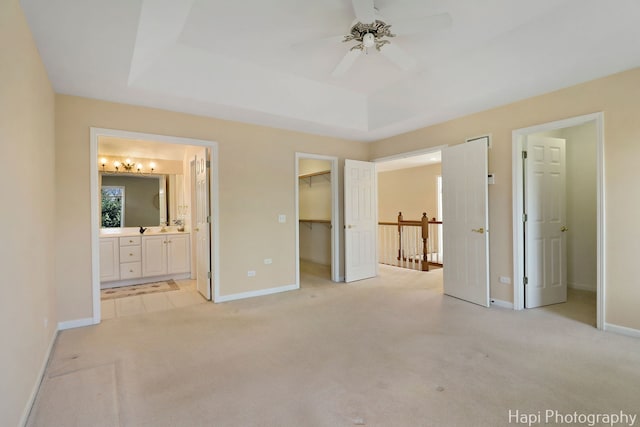 unfurnished bedroom featuring a closet, baseboards, a raised ceiling, a walk in closet, and light carpet