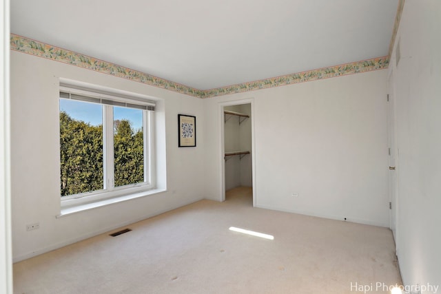 unfurnished bedroom featuring a spacious closet, carpet, visible vents, and a closet