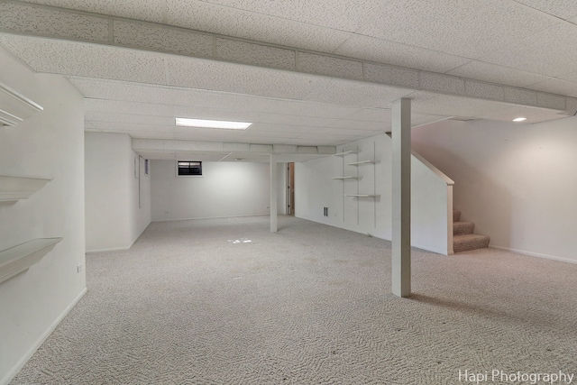 finished below grade area featuring carpet flooring, baseboards, a drop ceiling, and stairway