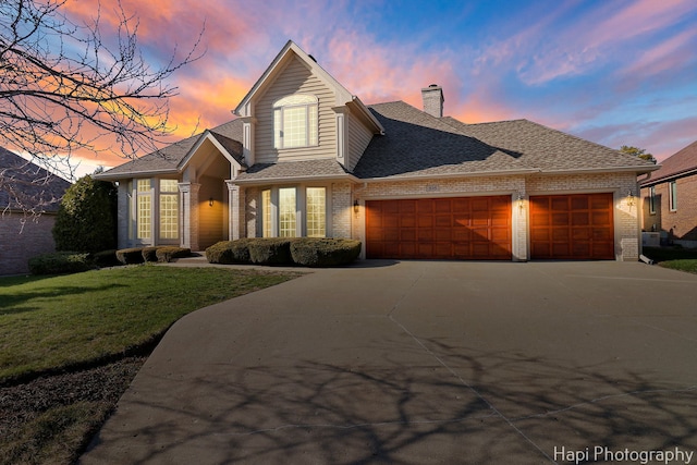 traditional home featuring a garage, a chimney, concrete driveway, brick siding, and a front lawn