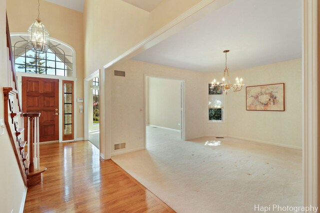 entrance foyer with wood finished floors, an inviting chandelier, a towering ceiling, and visible vents