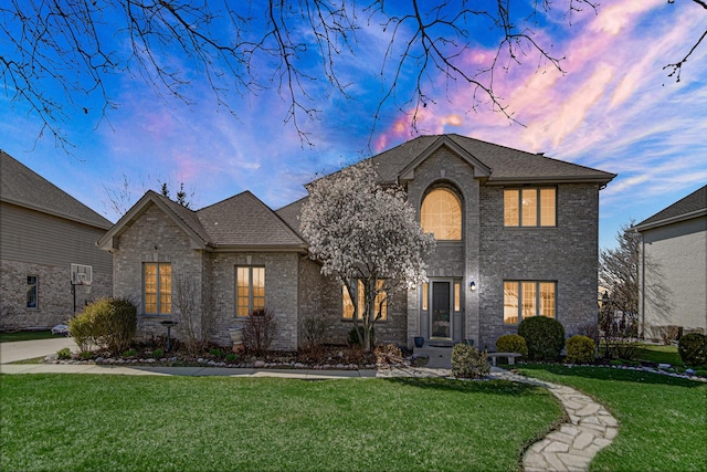 french country home featuring a yard, brick siding, and a shingled roof
