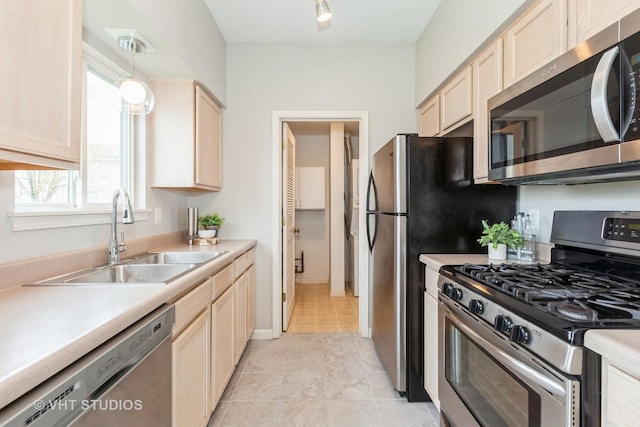 kitchen featuring light brown cabinets, a sink, stainless steel appliances, light countertops, and baseboards