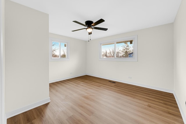 unfurnished room featuring a wealth of natural light, ceiling fan, baseboards, and wood finished floors