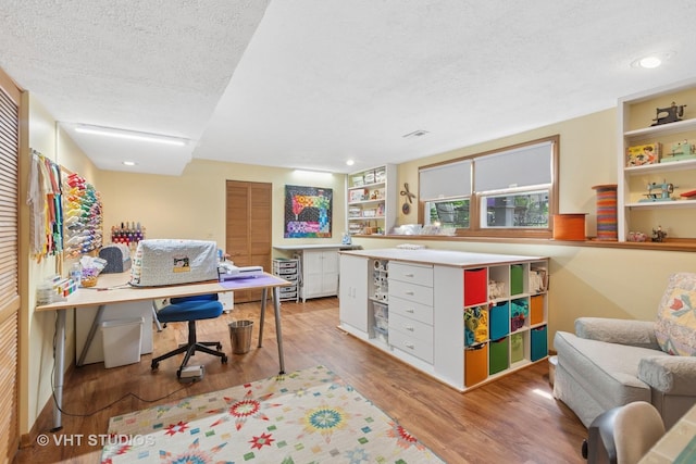 office space with a textured ceiling, light wood-style floors, built in shelves, and recessed lighting