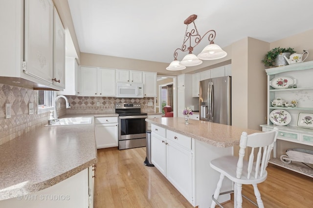 kitchen with stainless steel appliances, a sink, a kitchen island, light wood finished floors, and decorative backsplash