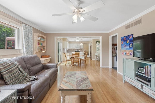 living area featuring a ceiling fan, light wood-type flooring, crown molding, and baseboards