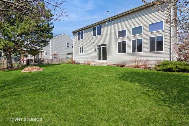 back of property with entry steps, fence, and a lawn