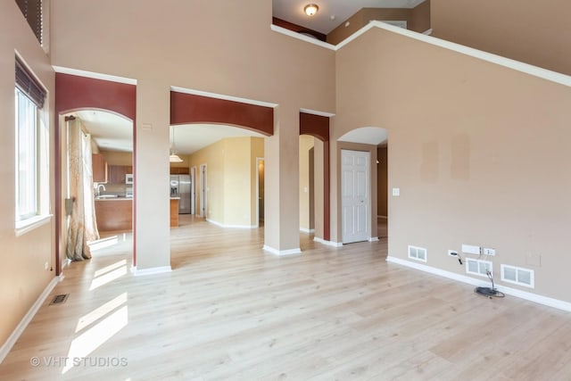 empty room featuring light wood-style flooring, arched walkways, and visible vents