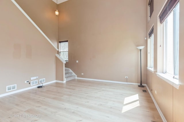 unfurnished living room featuring plenty of natural light, a towering ceiling, visible vents, and baseboards