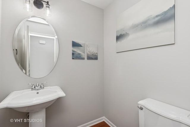 half bathroom with baseboards, a sink, toilet, and wood finished floors