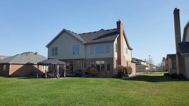 rear view of house with brick siding, a gazebo, and a lawn