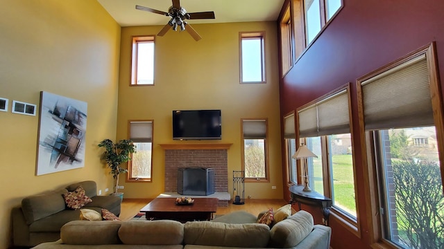 living room featuring wood finished floors, ceiling fan, a brick fireplace, visible vents, and a high ceiling