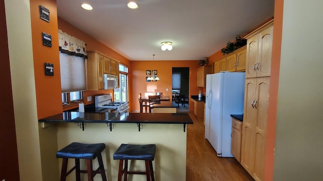 kitchen featuring white refrigerator with ice dispenser, stainless steel microwave, dark countertops, a peninsula, and range with gas cooktop