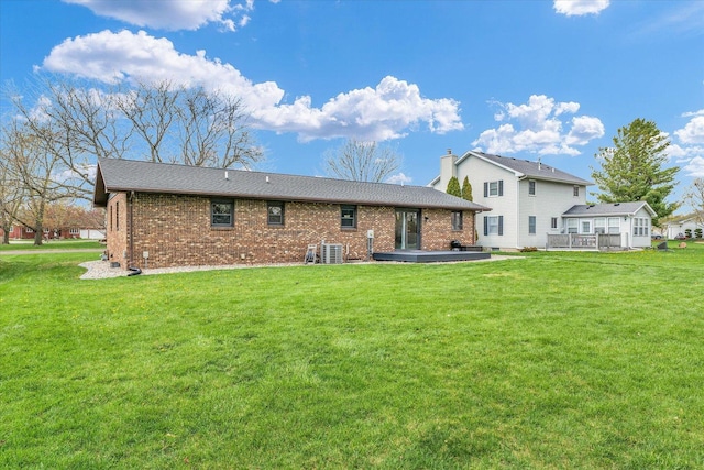 back of house with brick siding, a wooden deck, central AC, and a lawn