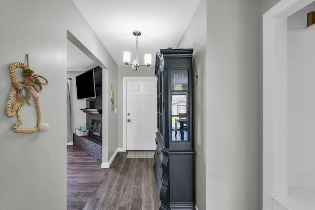 entrance foyer featuring dark wood-style flooring, baseboards, a notable chandelier, and a brick fireplace