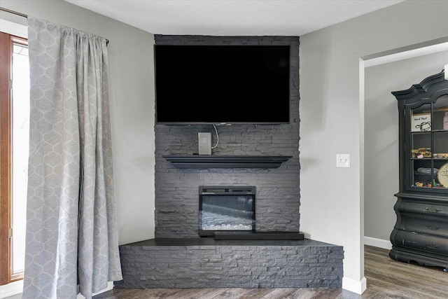 unfurnished living room featuring a stone fireplace, wood finished floors, and baseboards