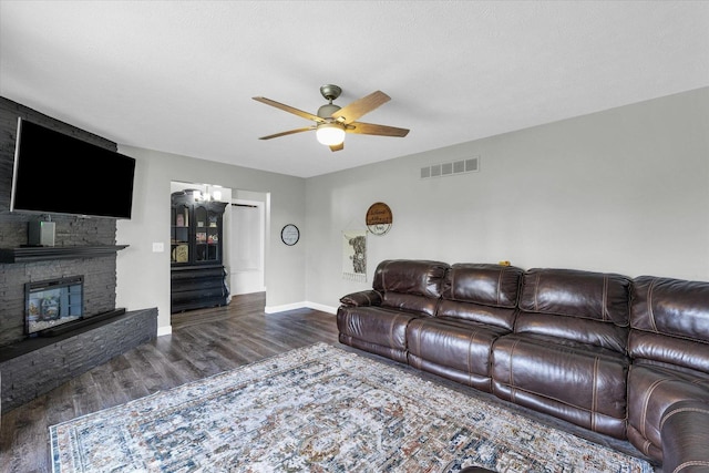 living area featuring baseboards, a stone fireplace, visible vents, ceiling fan, and wood finished floors