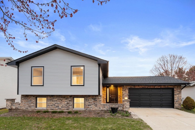 tri-level home featuring a front yard, an attached garage, a shingled roof, and concrete driveway