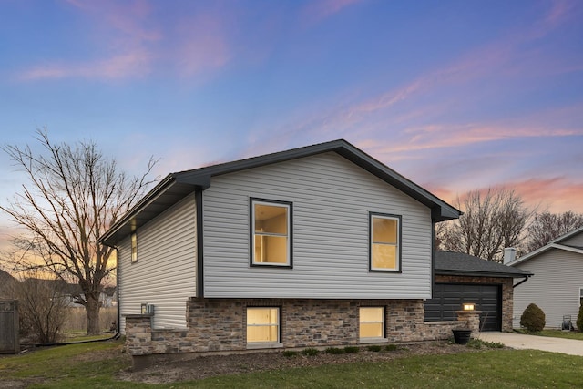 view of front of property featuring an attached garage, concrete driveway, stone siding, and a lawn