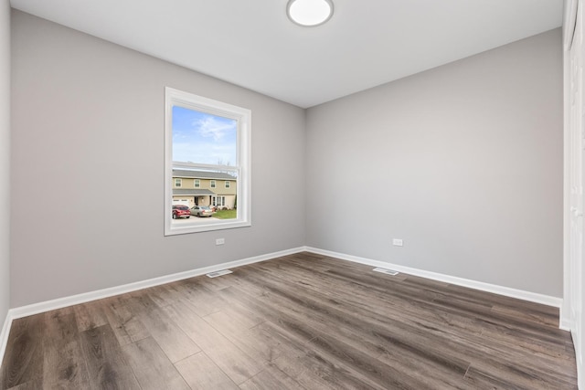 empty room with dark wood-style flooring, baseboards, and visible vents