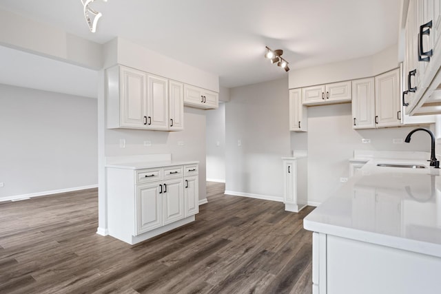 kitchen featuring white cabinets, baseboards, a sink, light countertops, and dark wood-style floors