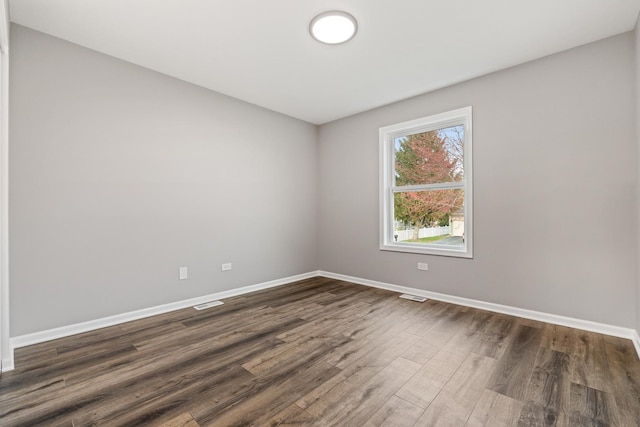 empty room with dark wood-style flooring, baseboards, and visible vents