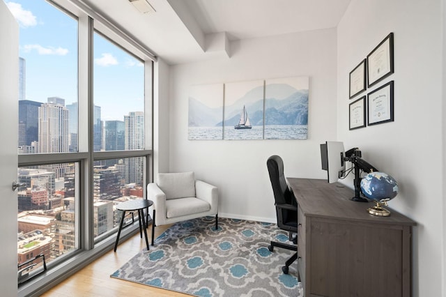 office space with wood finished floors, visible vents, baseboards, and a wall of windows