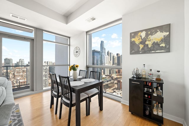 dining room with a city view, visible vents, wood finished floors, and a wall of windows