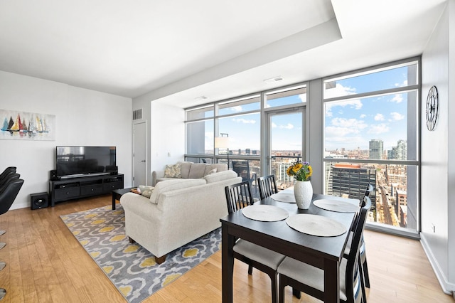 living area featuring visible vents, a wall of windows, light wood finished floors, and a view of city