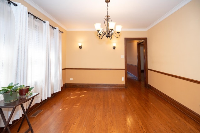 spare room with baseboards, an inviting chandelier, ornamental molding, visible vents, and wood finished floors