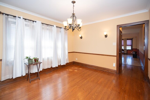 spare room with a notable chandelier, baseboards, crown molding, visible vents, and wood finished floors
