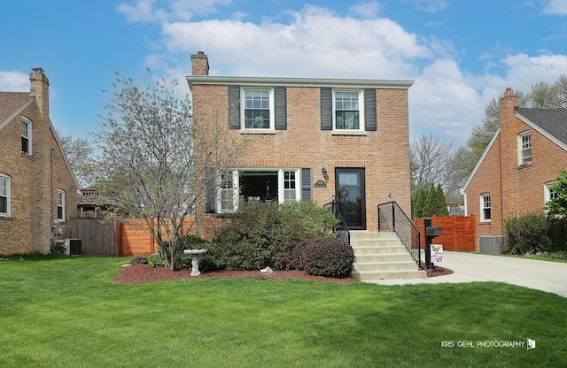 traditional-style house with fence, a front lawn, brick siding, a chimney, and central air condition unit
