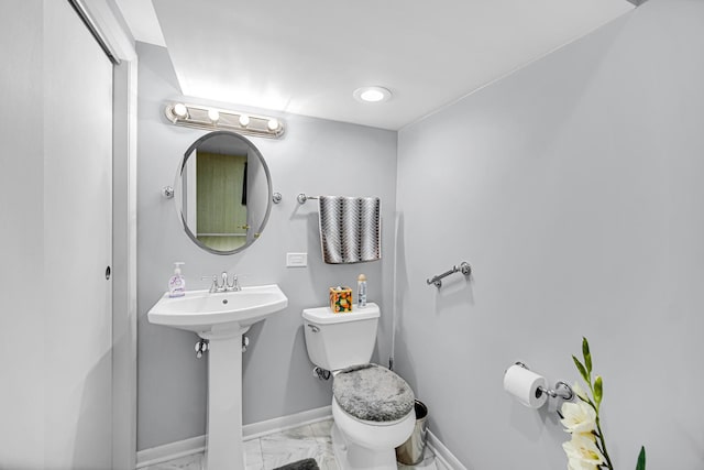 bathroom with marble finish flooring, baseboards, toilet, and a sink