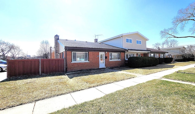 view of front of home with fence, a front yard, brick siding, and a chimney