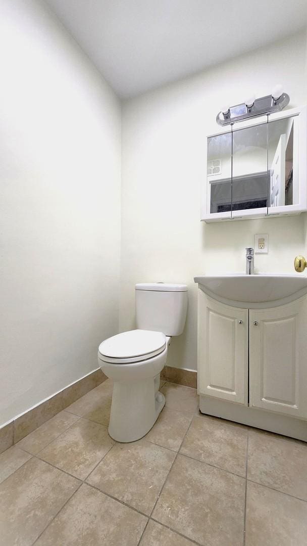 half bath with toilet, tile patterned floors, vanity, and baseboards