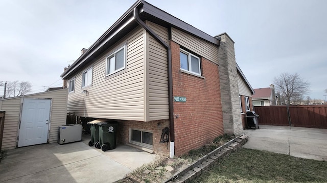 view of side of property with an outdoor structure, a chimney, a patio area, a storage shed, and fence