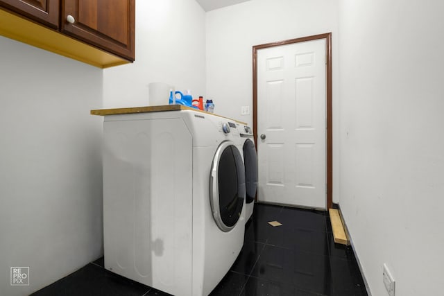 laundry area with dark tile patterned flooring, washer and clothes dryer, and cabinet space