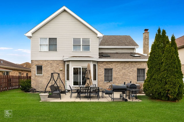 rear view of property featuring a chimney, a yard, fence, and brick siding